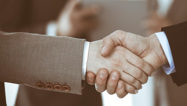 Mensen uit het bedrijfsleven handen schudden terwijl ze met collega's staan na ontmoeting of onderhandeling, close-up. Groep onbekende zakenlieden en vrouwen in modern kantoor. Teamwerk, partnerschap en handdrukconcept, getinte foto.