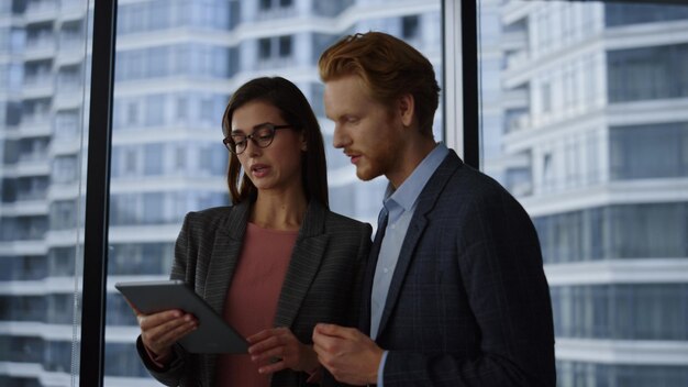 Mensen uit het bedrijfsleven met behulp van tablet-computer op kantoor Ernstige zakenpartners praten binnenshuis Bedrijfsmedewerkers bespreken nieuw project op digitale tablet Zakenpaar werkt in hoofdkantoor