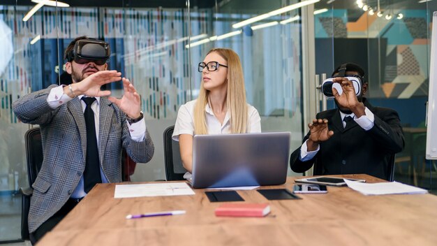 Mensen uit het bedrijfsleven met behulp van virtual reality-bril tijdens vergadering. Team van ontwikkelaars die virtual reality-headset testen en nieuwe ideeën bespreken om de visuele ervaring te verbeteren.