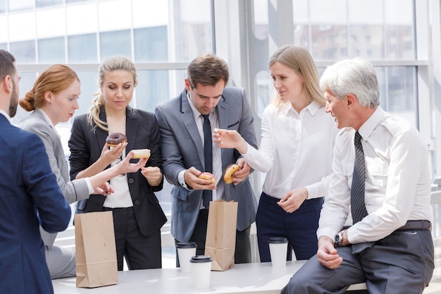 Mensen uit het bedrijfsleven met koffiepauze samen donuts eten op kantoor