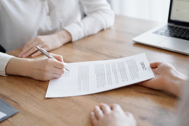 Foto mensen uit het bedrijfsleven ondertekenen contractpapieren terwijl ze aan de houten tafel zitten in kantoor, close-up. partners of advocaten die samenwerken tijdens de vergadering. teamwerk, partnerschap, succesconcept.