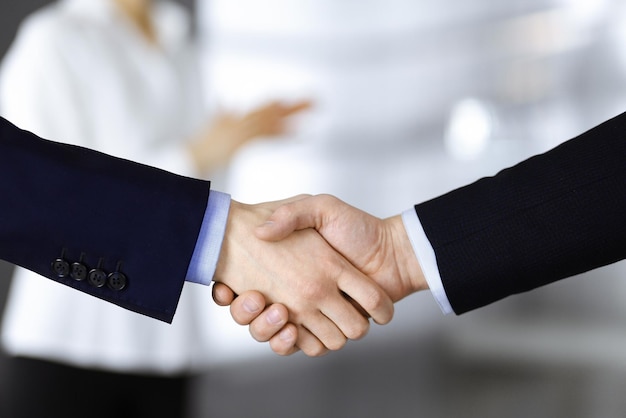 Mensen uit het bedrijfsleven schudden handen tijdens vergadering of onderhandeling, close-up. Groep onbekende zakenlieden en een vrouw in een modern kantoor. Teamwork, partnerschap en handdruk concept.