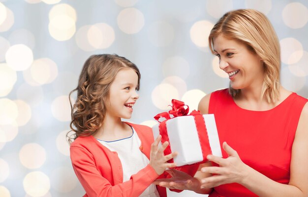 mensen, vakantie, kerstmis en familieconcept - gelukkige moeder en dochter die een geschenkdoos geven en ontvangen over de achtergrond van vakantieverlichting