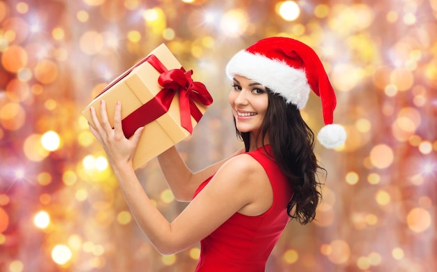 mensen, vakantie, kerstmis en vieringsconcept - mooie sexy vrouw in rode kleding en santahoed met giftdoos over lichtenachtergrond
