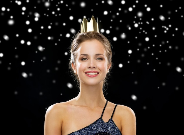 mensen, vakanties, royalty's en kerstconcept - glimlachende vrouw in avondjurk die gouden kroon draagt over zwarte besneeuwde achtergrond