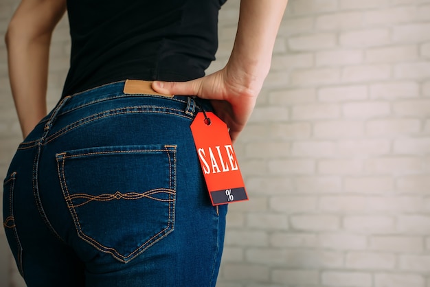 Mensen, verkoop, consumentisme concept. Close-up bijgesneden foto van seksuele vrouw billen dragen blauwe casual denim broek op grijze bakstenen achtergrond in het winkelcentrum. Rode tag Black Friday op jeans.