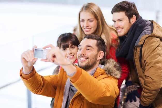 mensen, vriendschap, technologie en vrije tijd concept - gelukkige vrienden nemen selfie met digitale camera op ijsbaan