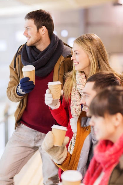 Mensen, vriendschap, warme dranken en vrije tijd concept - gelukkige vrienden drinken uit papieren koffiekopjes op de ijsbaan