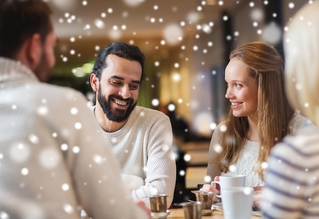 Foto mensen, vrije tijd, communicatie, seizoen en concept - gelukkige vrienden ontmoeten en drinken thee of koffie in het wintercafé