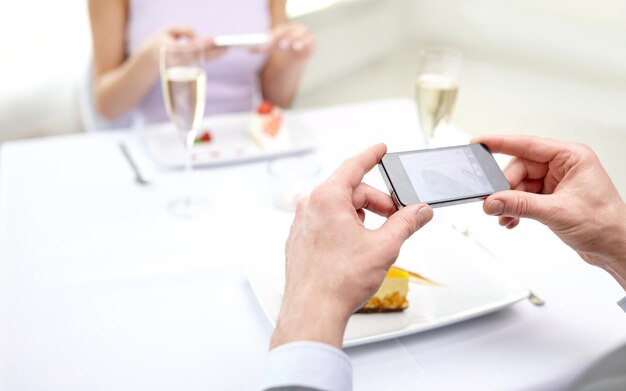 mensen, vrije tijd, eten en technologie concept - close-up van paar met smartphones die foto's maken van eten in restaurant