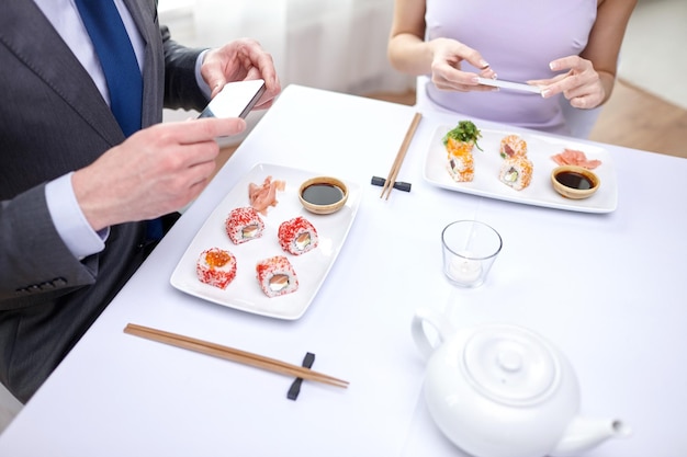 mensen, vrije tijd, eten, eten en technologie concept - close-up van een paar met smartphones die een foto maken van sushi in restaurant