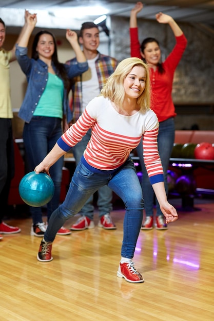 mensen, vrije tijd, sport en entertainment concept - gelukkige jonge vrouw die bal gooit in bowlingclub