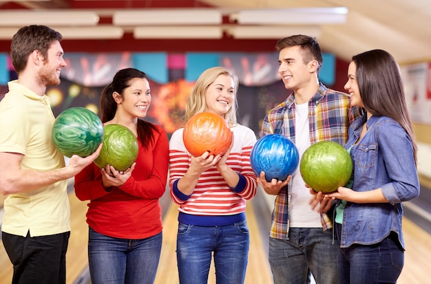 mensen, vrije tijd, sport, vriendschap en entertainment concept - gelukkige vrienden die ballen vasthouden en praten in een bowlingclub