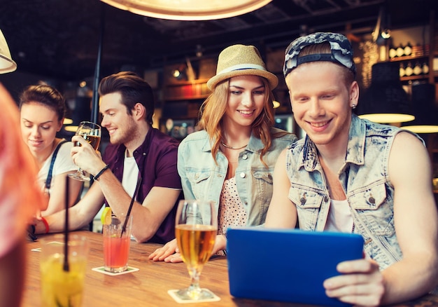 mensen, vrije tijd, vriendschap en communicatie concept - groep gelukkige lachende vrienden met tablet pc-computer en drankjes aan de bar of pub