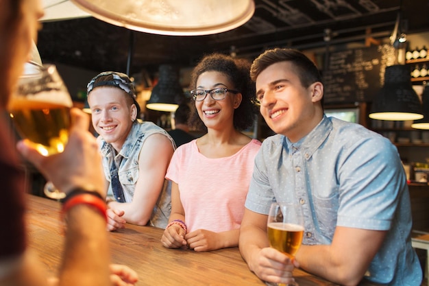 mensen, vrije tijd, vriendschap en communicatieconcept - groep gelukkige lachende vrienden die bier drinken en praten in de bar of pub