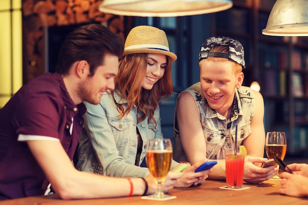 mensen, vrije tijd, vriendschap en communicatieconcept - groep gelukkige lachende vrienden met smartphones en drankjes aan bar of pub