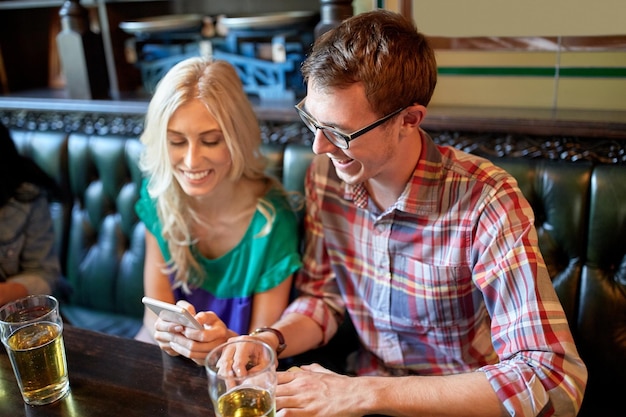 mensen, vrije tijd, vriendschap en communicatieconcept - vrienden met smartphones die bier drinken en sms'en in bar of pub