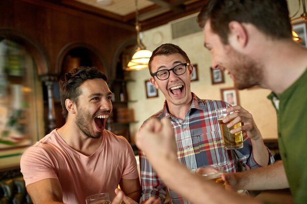 mensen, vrije tijd, vriendschap en entertainment concept - gelukkige voetbalfans of mannelijke vrienden die bier drinken en de overwinning vieren in de bar of pub