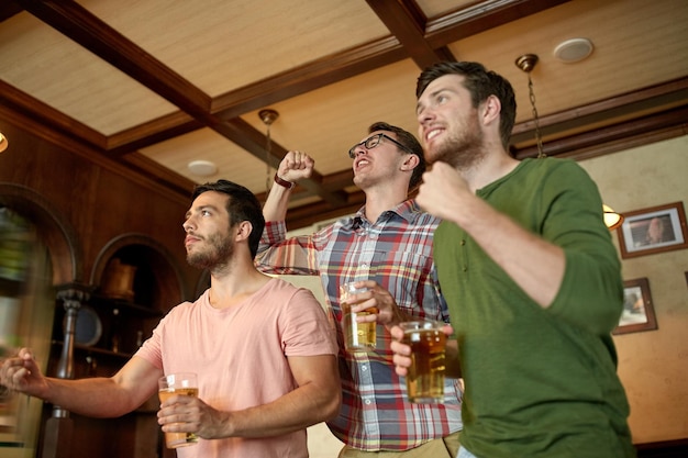 Foto mensen, vrije tijd, vriendschap en sportconcept - gelukkige mannelijke vrienden of fans kijken naar sportwedstrijden of voetbalwedstrijden en drinken bier in de bar of pub