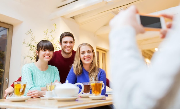 mensen, vrije tijd, vriendschap en technologie concept - groep gelukkige vrienden met smartphone die foto's maakt en thee drinkt in café