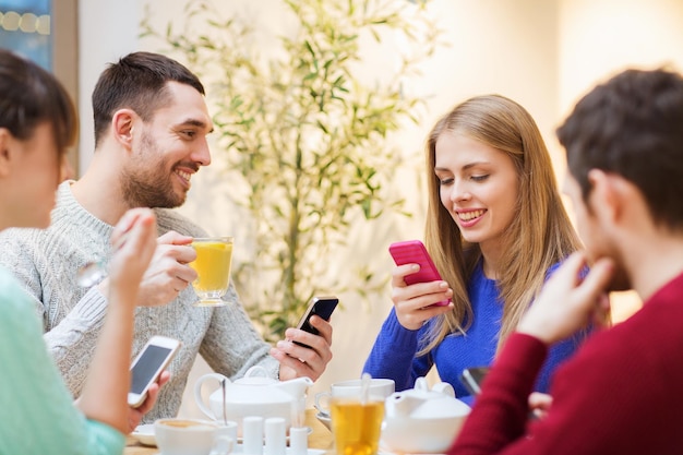 mensen, vrije tijd, vriendschap en technologie concept - groep gelukkige vrienden met smartphones ontmoeten elkaar in café en drinken thee