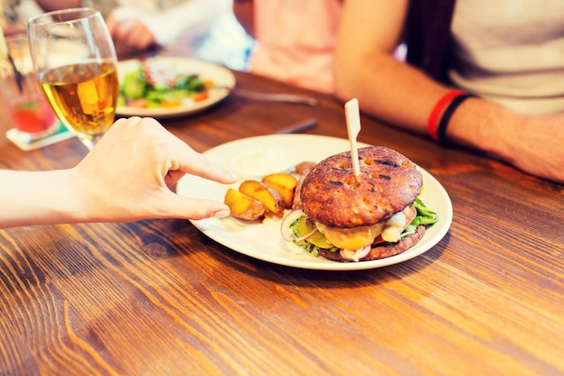 mensen, vrije tijd, vriendschap, eten en eten concept - close-up van vrienden handen met hamburger in bar of pub