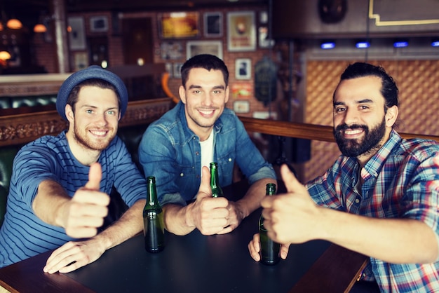 mensen, vrije tijd, vriendschap, gebaar en vrijgezellenfeestconcept - gelukkige mannelijke vrienden die gebotteld bier drinken en duimen opdagen bij bar of pub