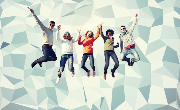 mensen, vrijheid, geluk en tienerconcept - groep gelukkige vrienden die in zonnebril hoog over grijze laag polyachtergrond springen