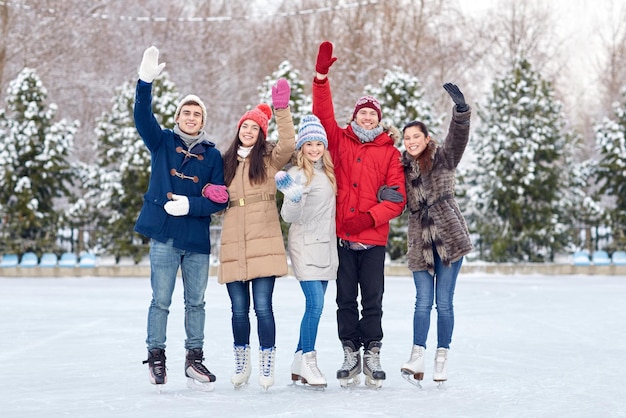 mensen, winter, vriendschap, sport en vrije tijd concept - gelukkige vrienden schaatsen en zwaaiende handen op de ijsbaan buitenshuis