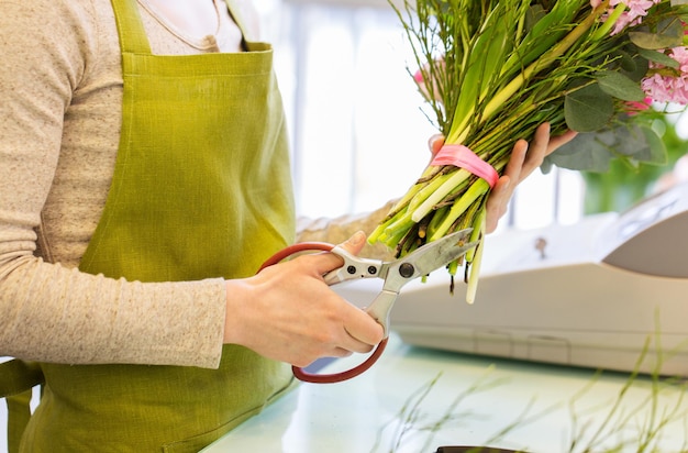 mensen, zaken, verkoop en bloemisterij concept - close-up van bloemist vrouw die bos maakt en stelen bijsnijdt met een schaar in bloemenwinkel