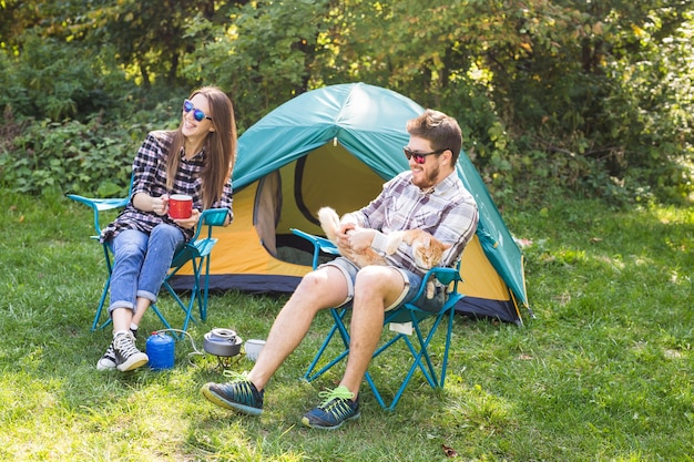 mensen, zomertoerisme en natuur concept - jong koppel zit in de buurt van een tent