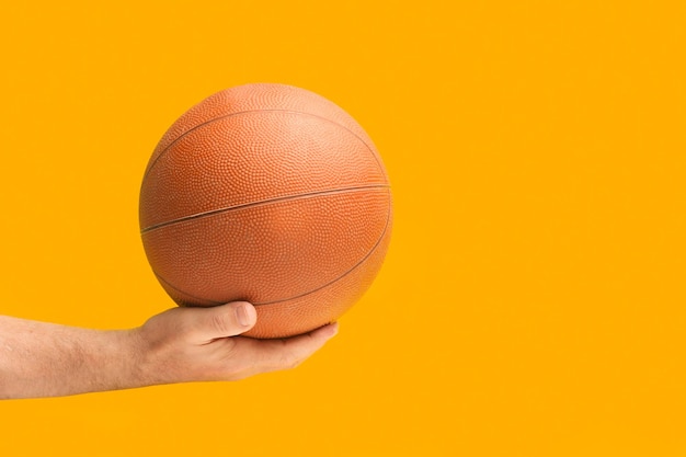 Mensenhand die een basketbalbal op een oranje achtergrond met exemplaarruimte houden