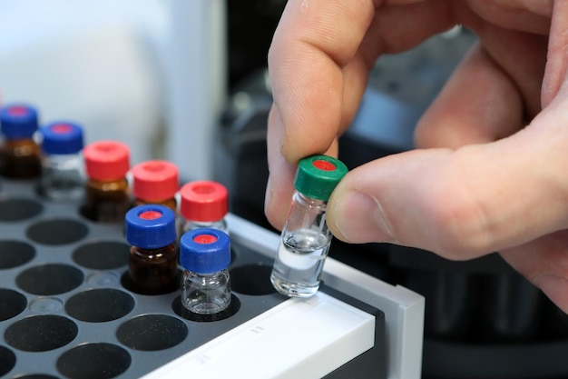 Mensenhand die een reageerbuisflesjes vasthoudt voor analyse in de gasvloeistofchromatograaf Laboratoriumassistent die glazen laboratoriumfles in een chromatograafflesje steekt