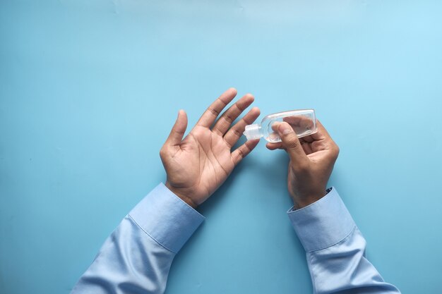 Mensenhand die ontsmettingsgel gebruikt om virus op blauwe backgorund te verhinderen