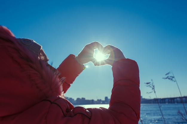 Mensenhanden die een liefdesteken over een zonachtergrond gebaren