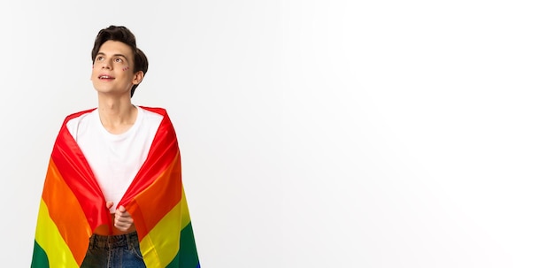 Mensenrechten en lgbtq-gemeenschap concept mooie androgyne jongeman met glitter op gezicht dragen regenboog trots vlag en kijken naar de linker bovenhoek witte achtergrond
