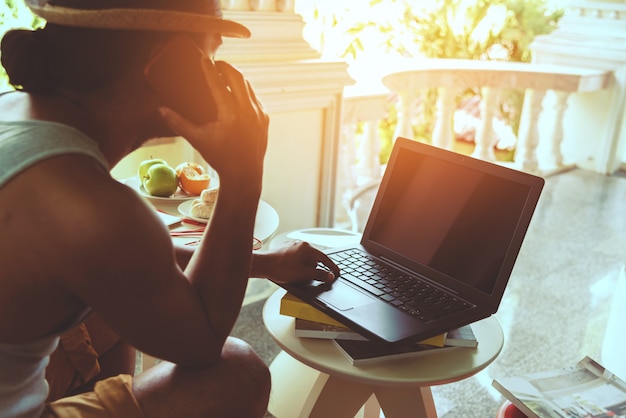 Mensenzitting die de mobiele telefoon spreekt en met laptop werkt