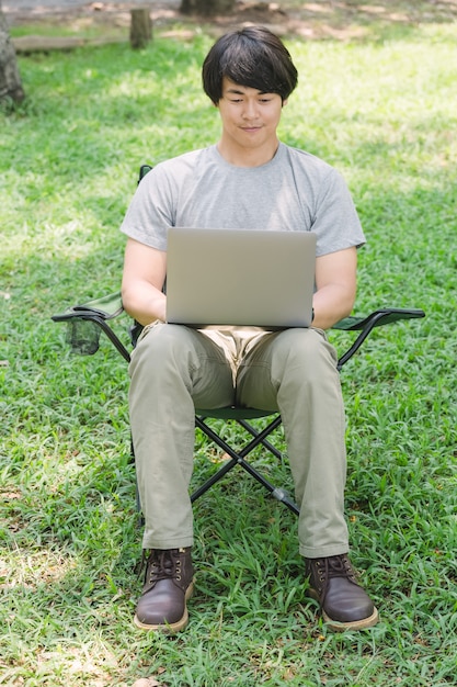 Mensenzitting op het kamperen stoel en het werken met laptop computer in de tuin