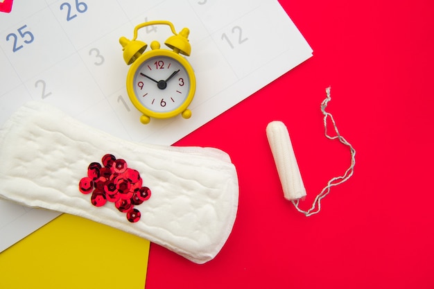 Menstrual calendar with feminine products and yellow alarm clock on colorful