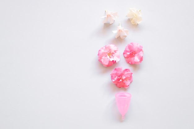 Menstrual cup and flowers over light background.