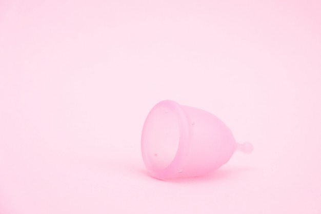 사진 분홍색 배경에 생리 컵입니다. 해당 기간 동안 대체 여성 위생 제품. 여성 건강 개념.