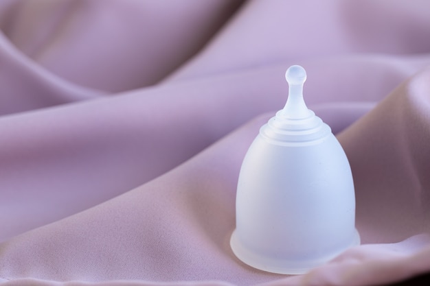 Menstrual cup on pink silk fabric close up photo