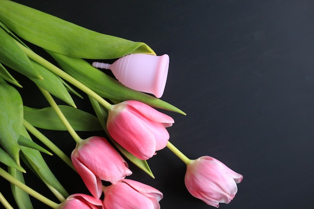 Menstrual cup and pink tulips on a black background. Women's health.