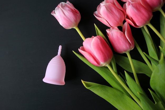 Menstrual cup and pink tulips on a black background.