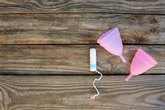 Menstrual cup and tampons on old wooden background. Top view.