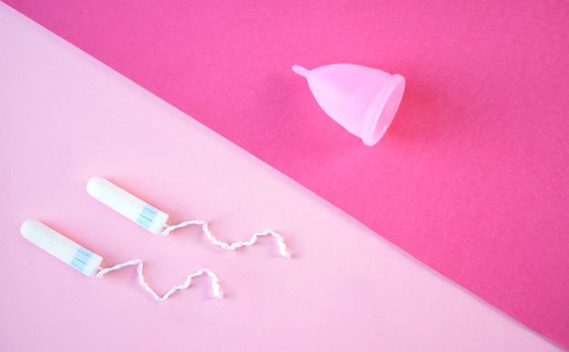 Photo menstrual cup and two tampons on a twocolored pink background the concept of menses