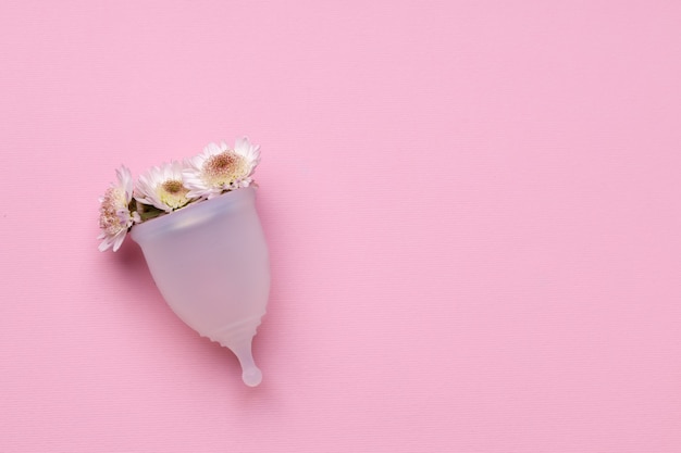 Menstrual cup with flowers on pink surface