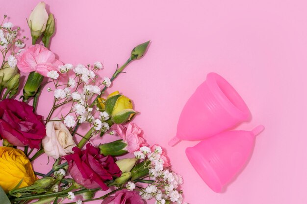生理カップは生気に優しい女性用製品を描いたピンクの背景に鮮やかな新鮮な花のコレクションに隣接しています