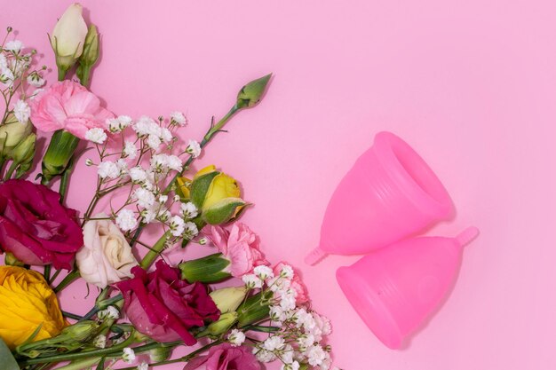 Photo menstrual cups beside a collection of vibrant fresh flowers on a pink background depicting an ecofriendly feminine product