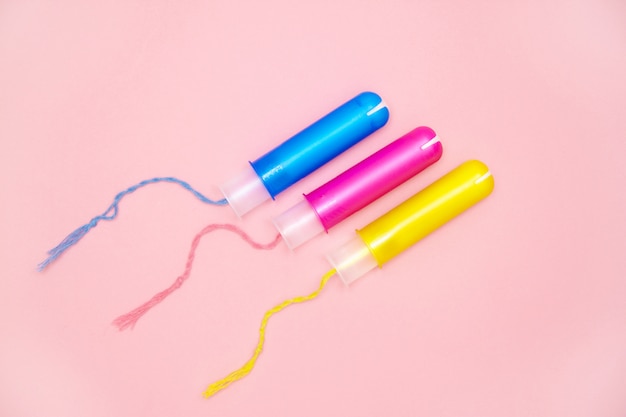 Photo menstrual cycle three cotton tampons with blue pink yellow applicartors on pink